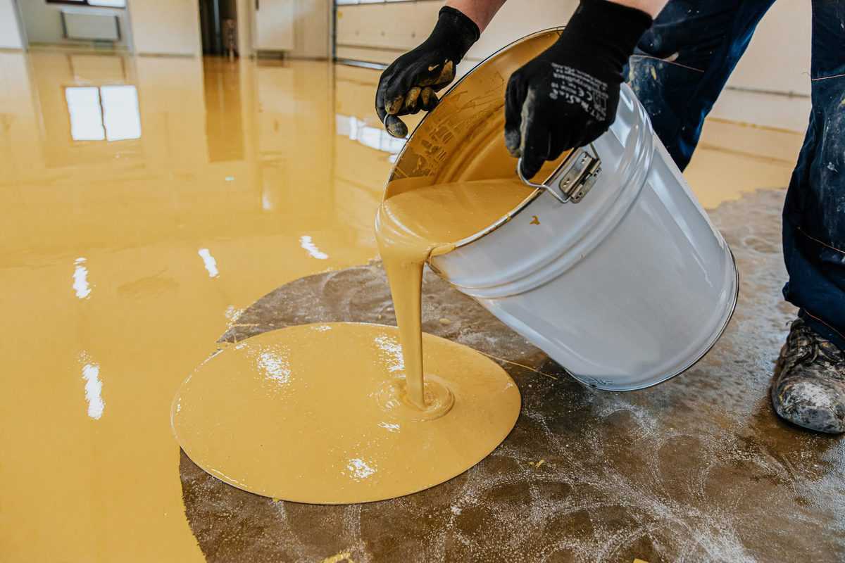 Yellow epoxy floor paint being poured onto a concrete surface for a smooth finish.