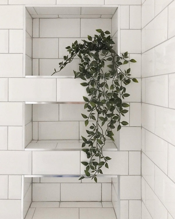 White tiled bathroom recessed shelf with a trailing green plant.