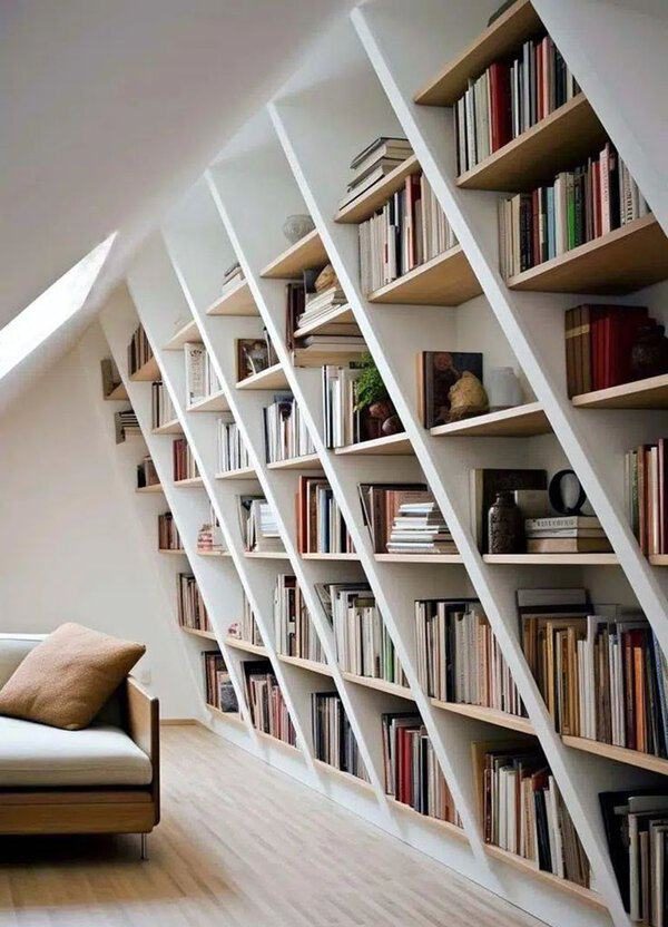 Slanted built-in bookshelves in a modern attic reading nook with a minimalist sofa.