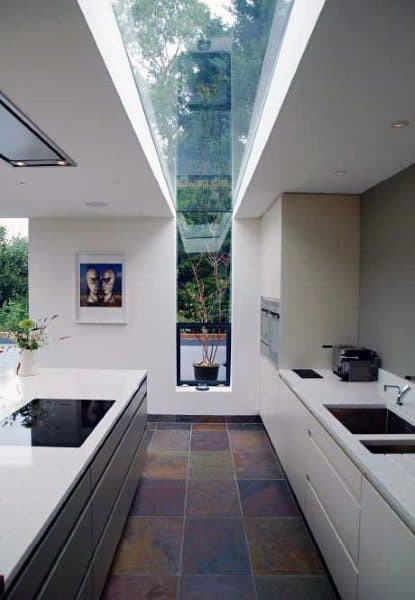 Modern kitchen with skylight, floor-to-ceiling glass window, white cabinets, and slate flooring.