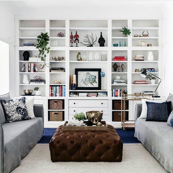 Living room with white bookshelves, gray sofas, and a brown tufted ottoman centerpiece