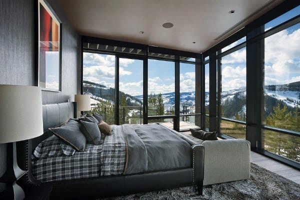 Cozy bedroom with floor-to-ceiling windows, plush rug, and panoramic snowy mountain views.