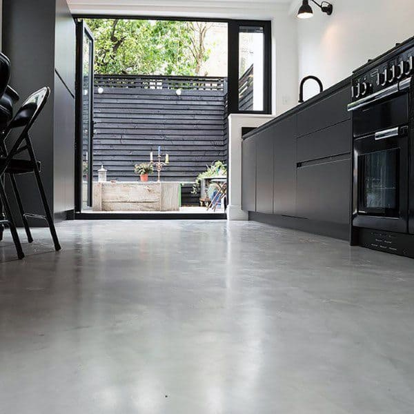 Modern kitchen with black cabinets, concrete floor, and open doors leading to a garden patio with plants and seating