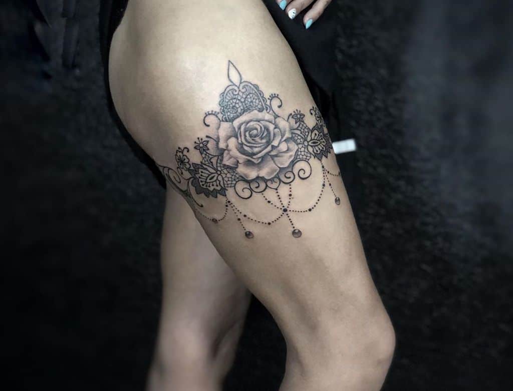 Thigh tattoo featuring an ornate rose with lace details, a decorative candle, and elegant beaded chain accents.