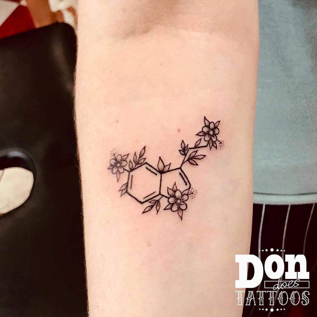 Tattoo of a serotonin chemical structure intertwined with delicate flowers on an arm