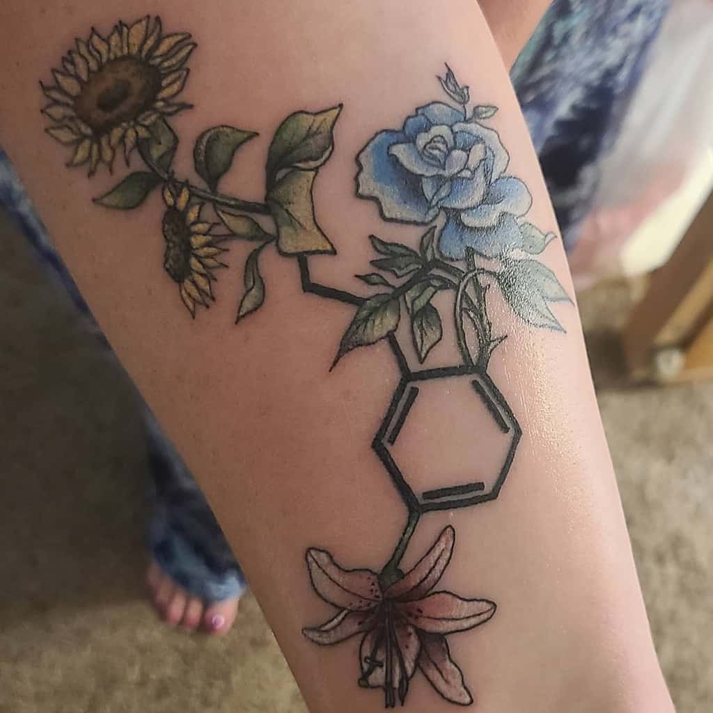 Serotonin molecule tattoo intertwined with a sunflower, blue rose, and pink lily on the forearm