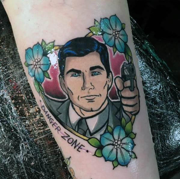 Detailed Archer tattoo featuring the spy aiming a gun, framed by blue flowers and a 'Danger Zone' banner, with a bold red background.