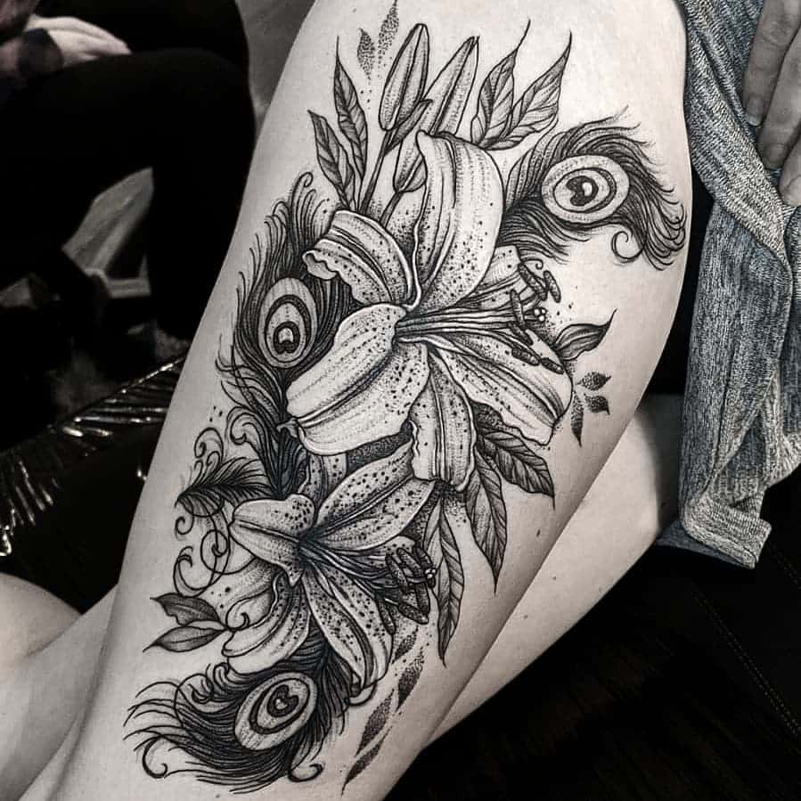 Black and grey thigh tattoo featuring detailed lilies intertwined with peacock feathers, showcasing fine linework, shading, and intricate patterns.