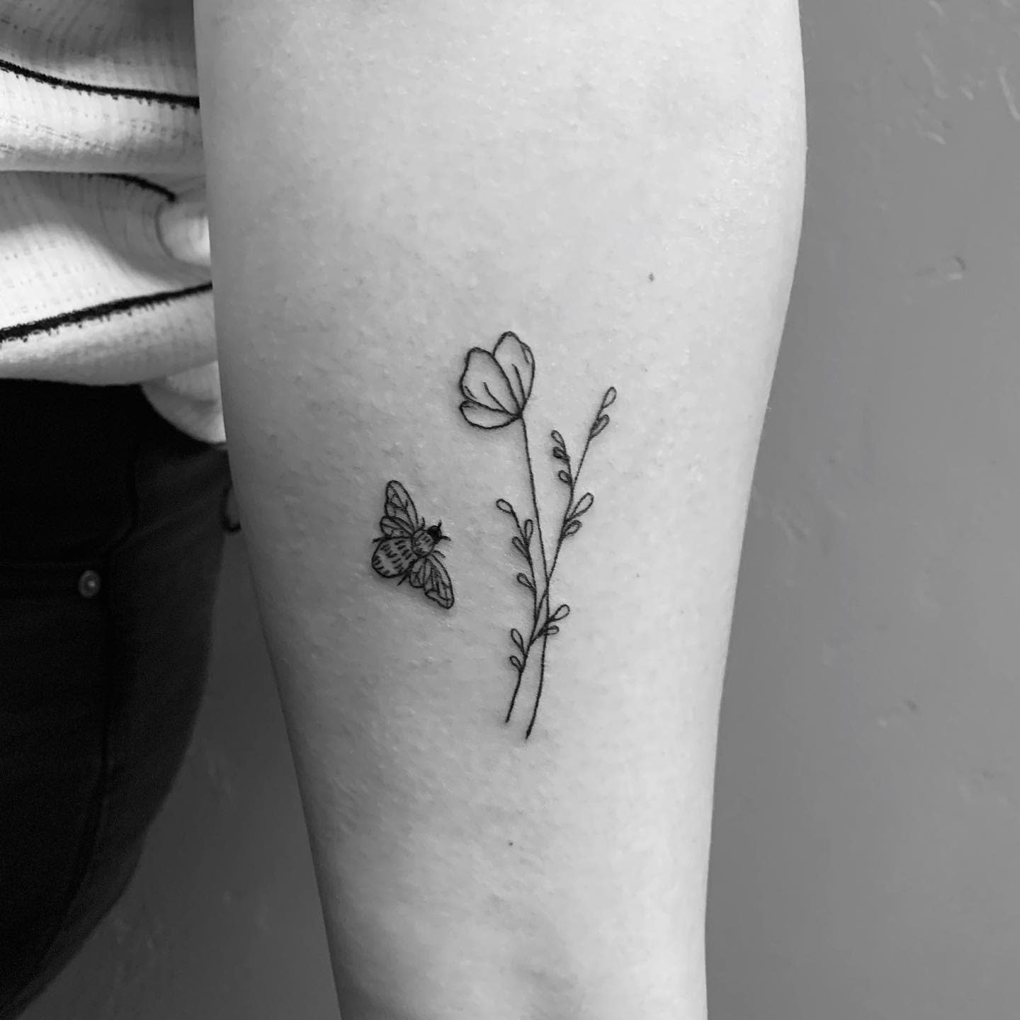 Minimalist tattoo of a butterfly, flower, and stem with leaves