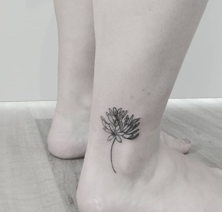 Minimalistic black line tattoo of a single flower with delicate petals and a long stem