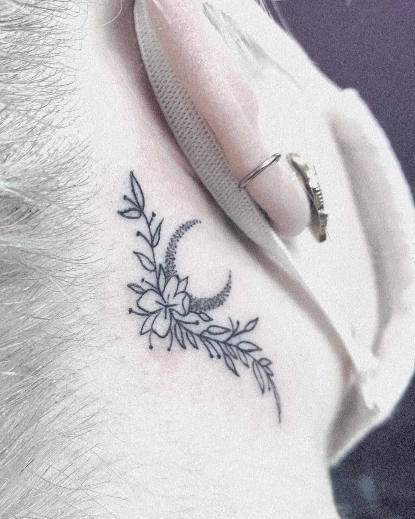 Small black tattoo of a crescent moon with flowers and leaves
