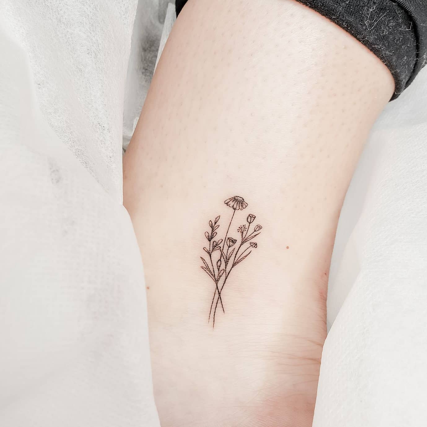Minimalist black line tattoo of delicate wildflowers
