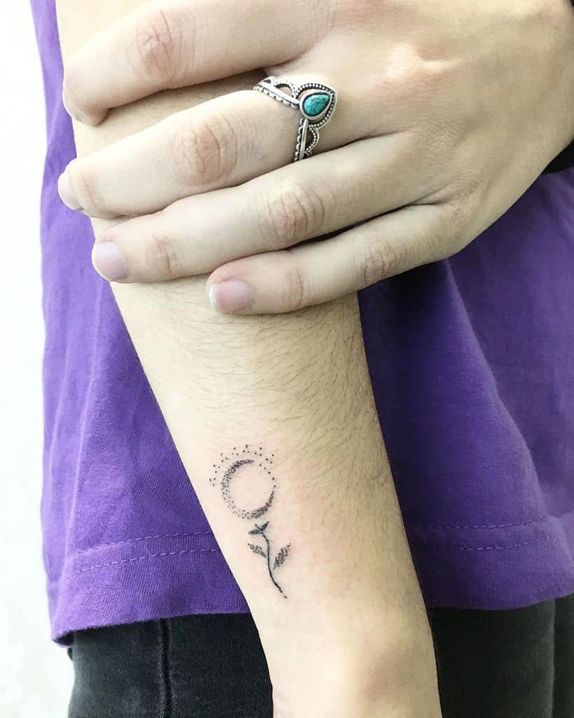 Minimalistic black ink tattoo featuring a flower with a circular shape formed by small dots, accompanied by a delicate stem and leaves