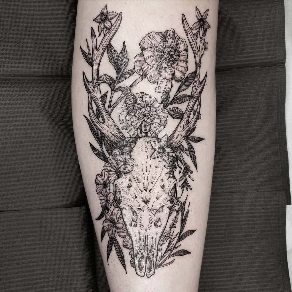 Tattoo of a deer skull with antlers, intricately surrounded by delicate flowers and lush foliage, beautifully inked on an arm