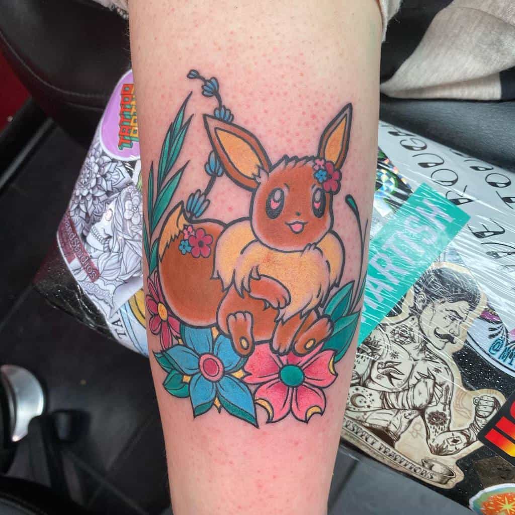 Playful Eevee tattoo surrounded by vibrant blue and pink flowers, featuring charming floral and leaf accents