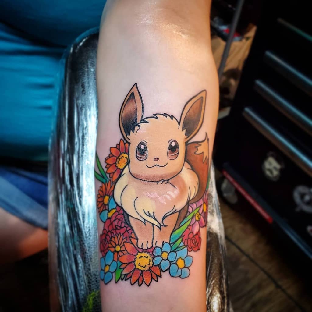 Bright and colorful Eevee tattoo surrounded by vibrant flowers in shades of orange, blue, and red for a lively, nature-inspired design