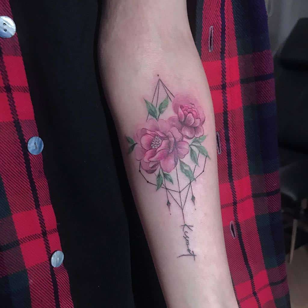 Delicate floral tattoo featuring pink roses with green leaves intertwined with geometric lines, and the word 'Kismet' elegantly written below