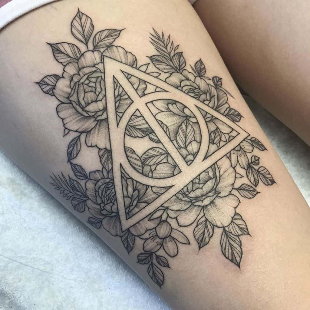 Deathly Hallows tattoo on the thigh with an intricate floral design, featuring detailed roses and leaves in fine black ink shading.