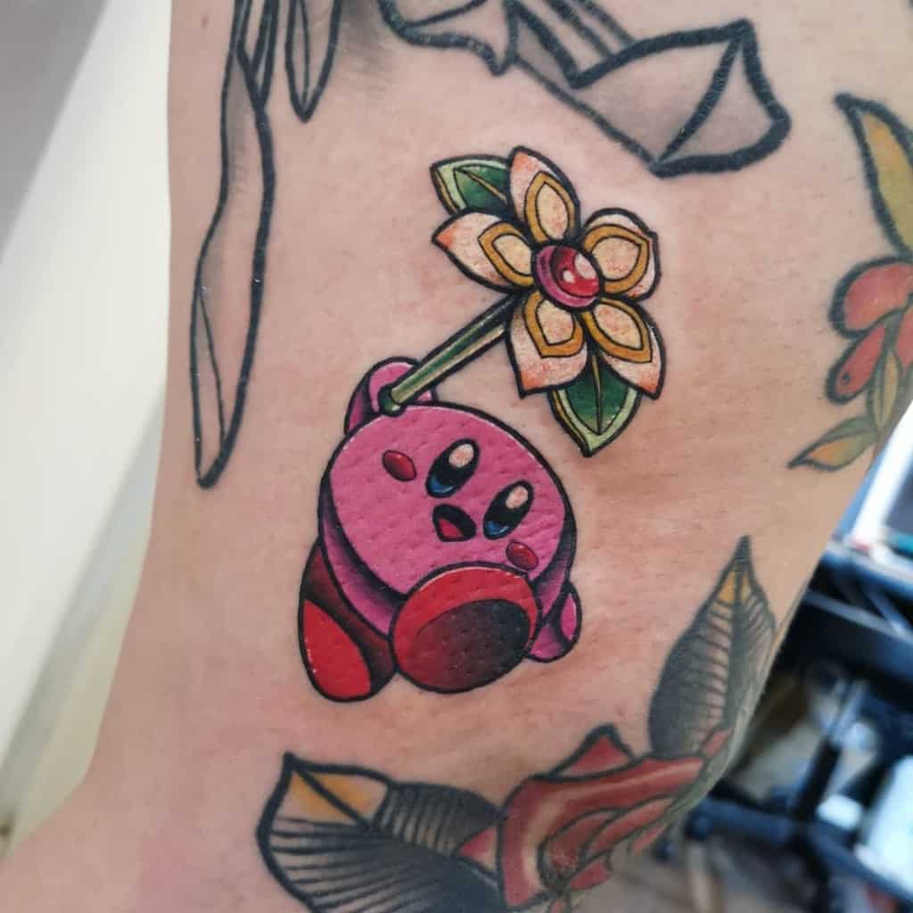 Kirby tattoo hanging onto a detailed flower and leaves with a jeweled center