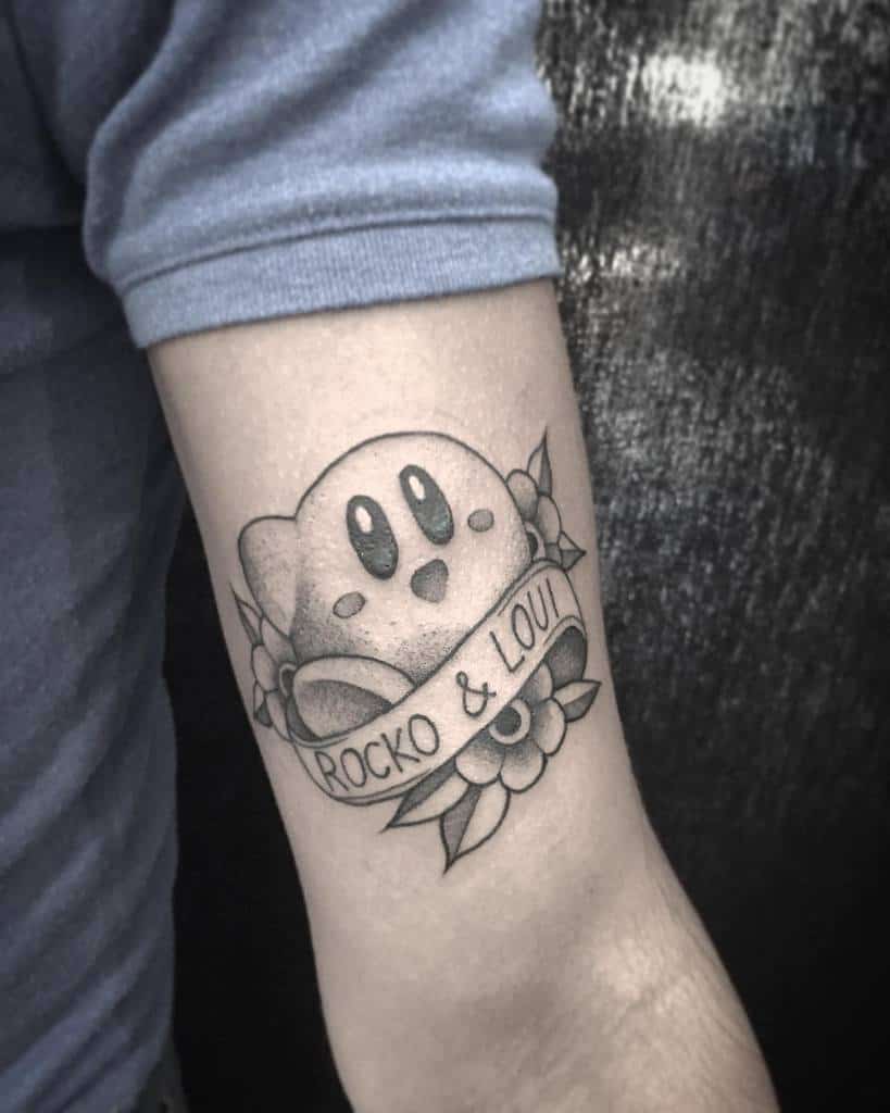 Black and grey Kirby tattoo with a banner reading "Rocko & Loui," surrounded by flowers and leaves