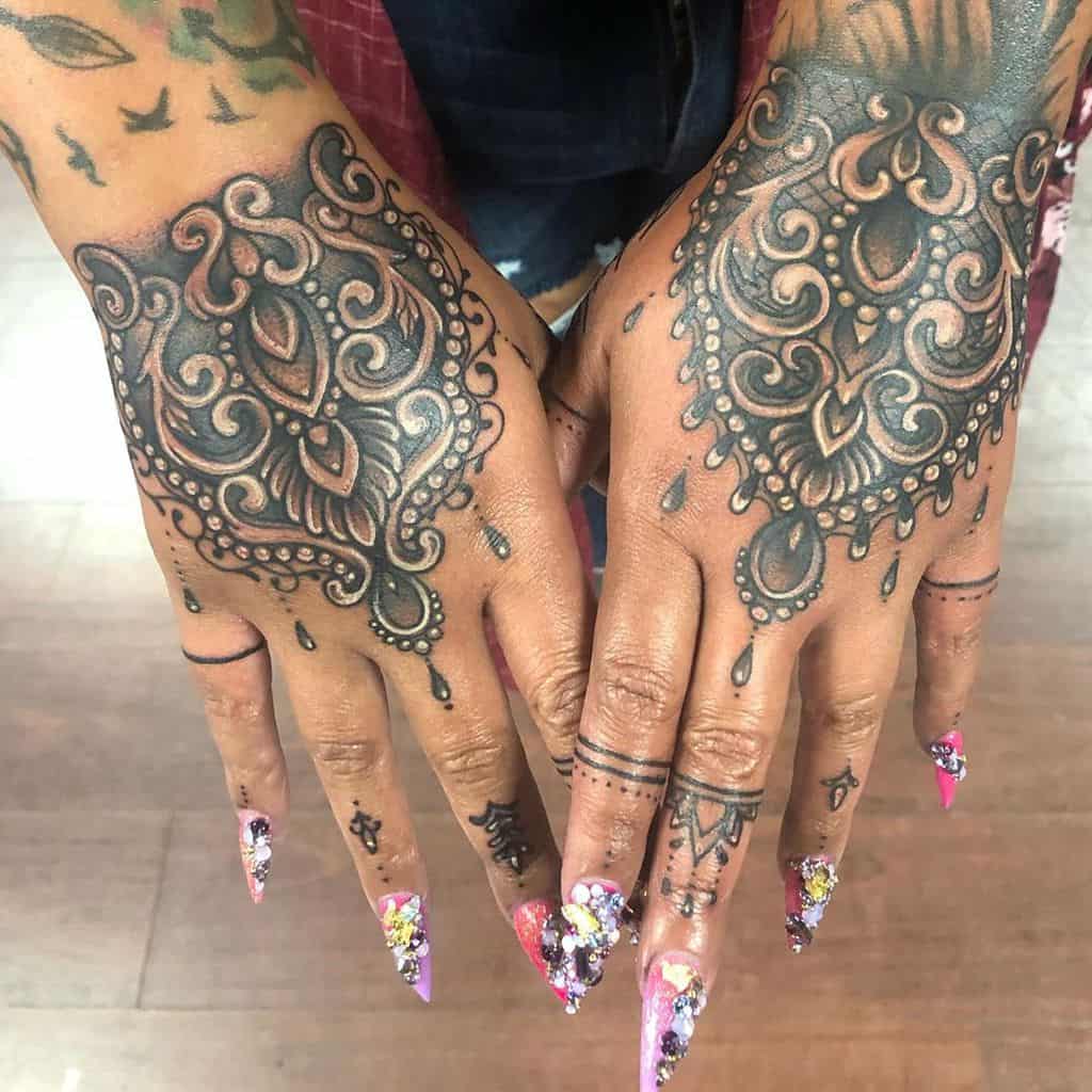 Intricate black ink hand tattoos featuring symmetrical ornamental lace patterns with delicate filigree and beaded details.