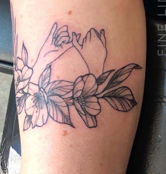 Tattoo of two hands forming a pinky swear, surrounded by flowers and leaves on an arm
