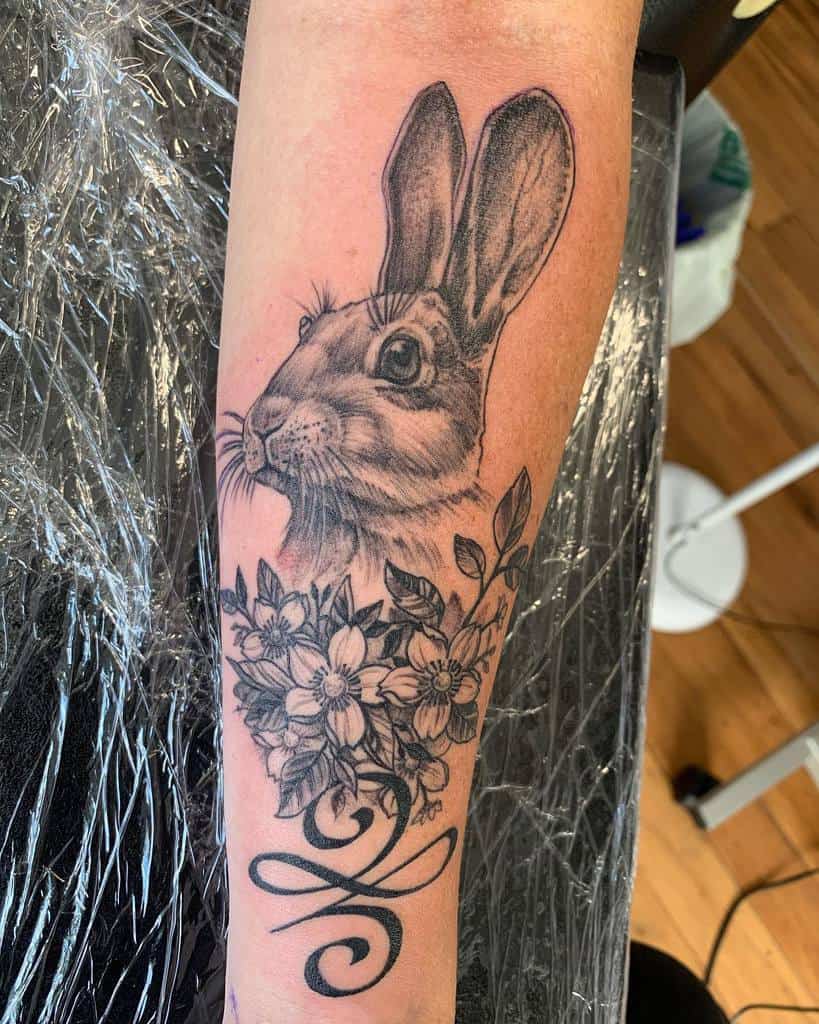 Black and gray tattoo of a rabbit surrounded by flowers with a swirl design