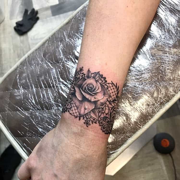 Elegant black and grey tattoo of a detailed rose with lace-like patterns and ornamental floral designs, accented with small white highlights