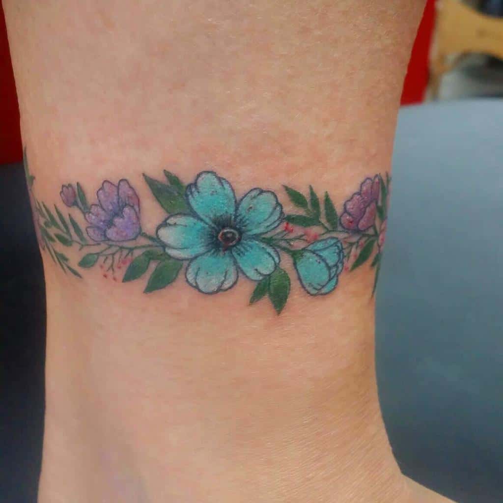 Delicate floral bracelet tattoo, featuring blue and purple flowers with green leaves in a soft, watercolor style