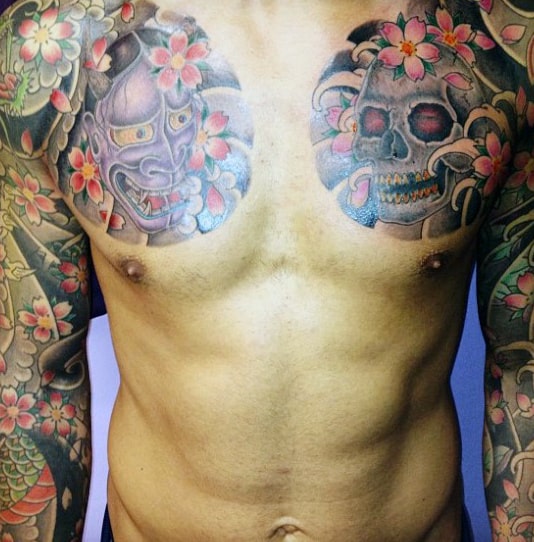 Tattooed chest with floral designs and masks, extending to full sleeve tattoos