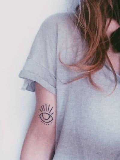 Minimalist tattoo of an eye with radiating lines, inked in black on the upper arm.