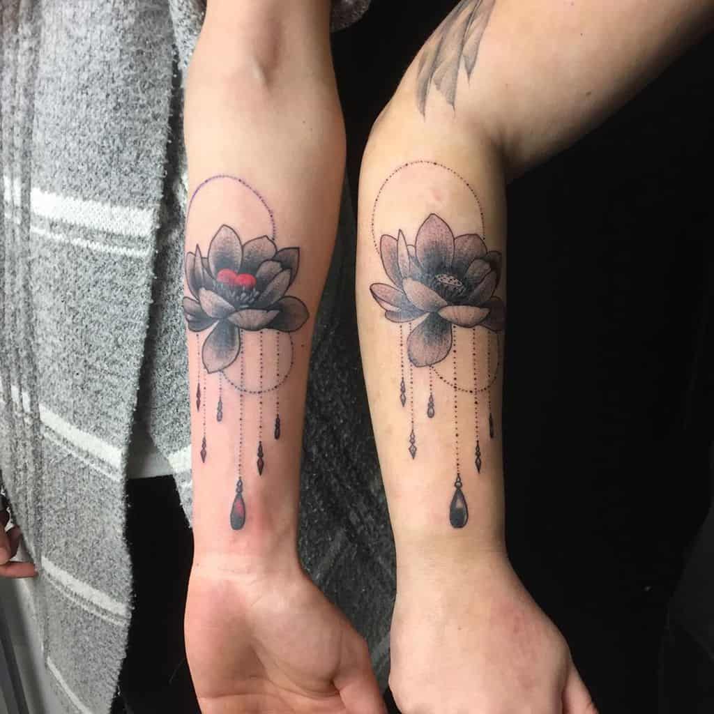 Matching sister tattoos featuring shaded lotus flowers with elegant dotted lines, beads, and subtle decorative elements