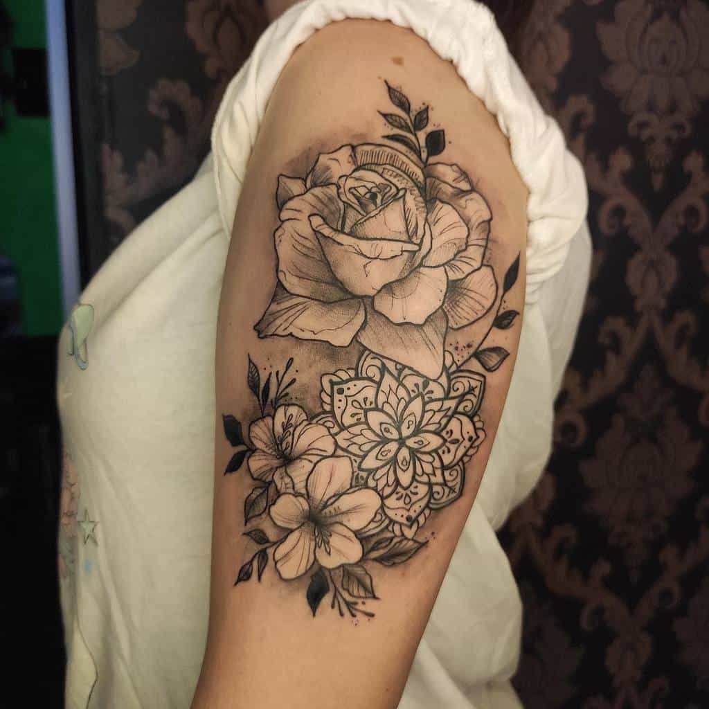 A detailed black rose and mandala tattoo on an upper arm, surrounded by smaller flowers and leaves