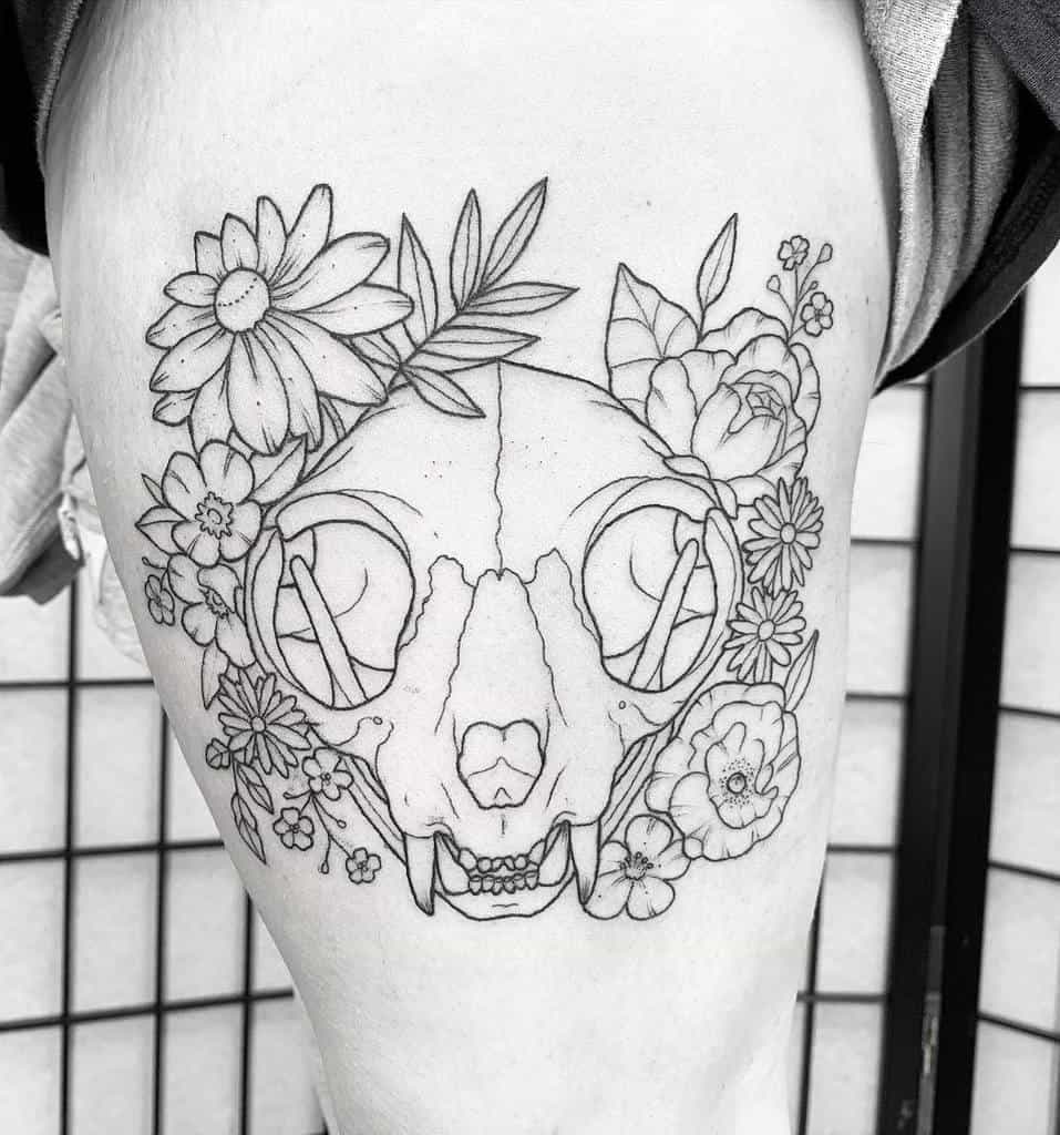 Line tattoo of a cat skull beautifully surrounded by flowers and leaves on a thigh
