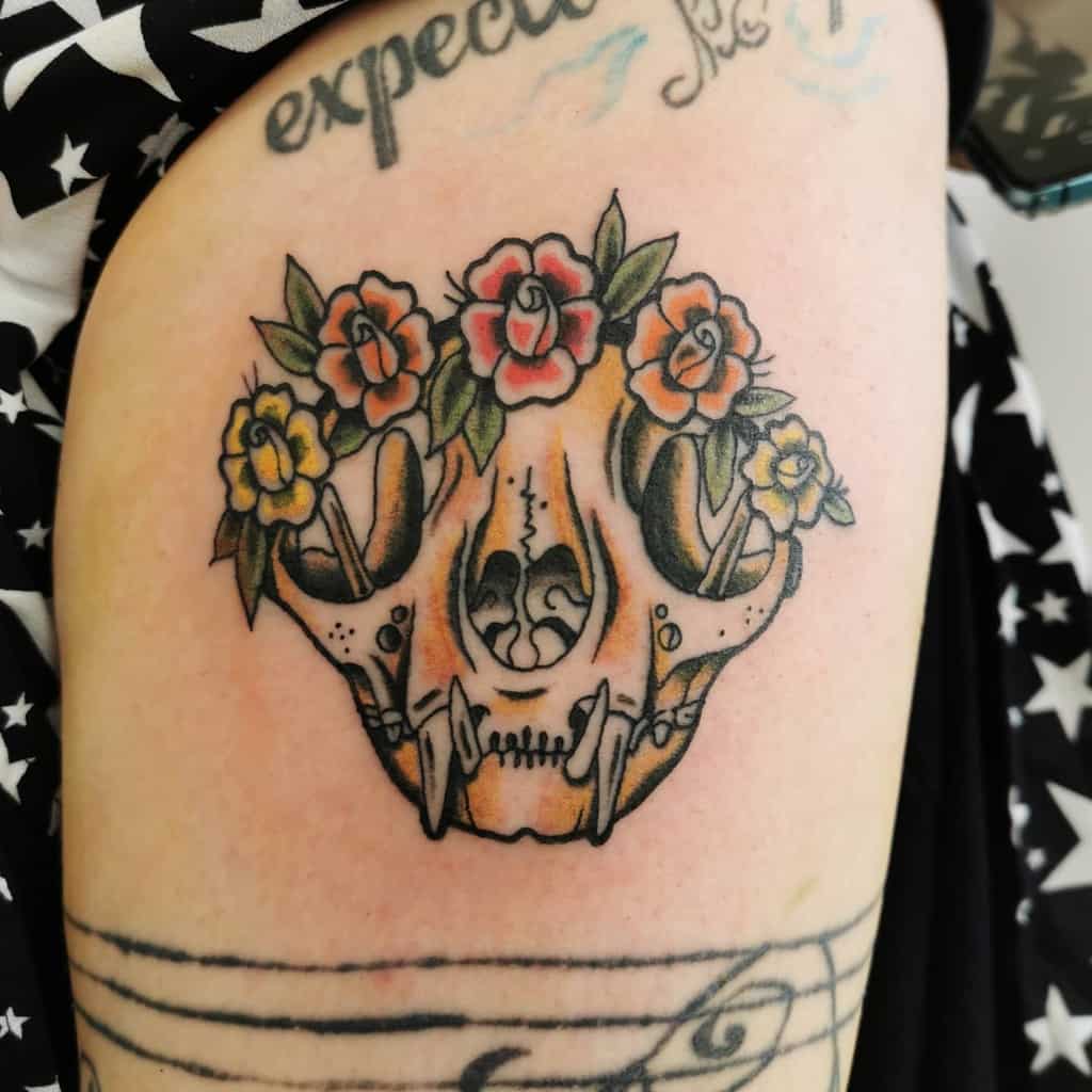 Colorful tattoo of a cat skull adorned with colorful flowers on an arm