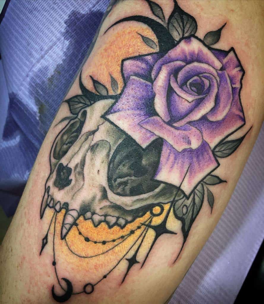 Tattoo of a cat skull with a purple rose, moon, and decorative elements on an arm