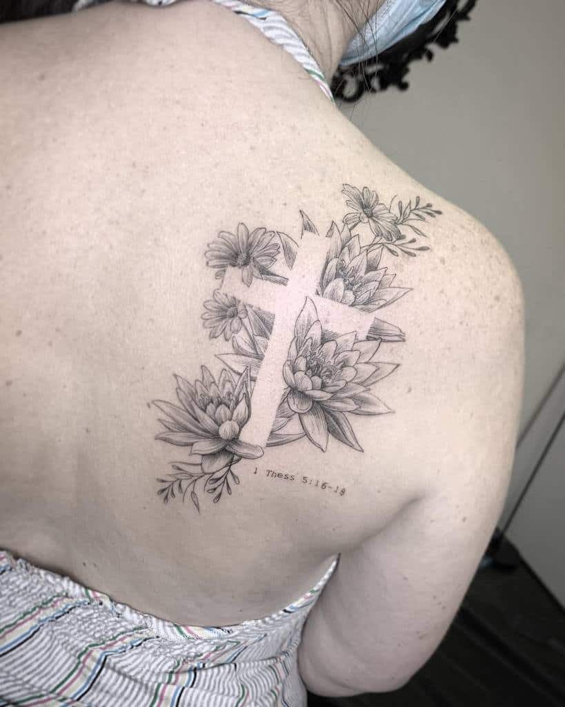A beautifully intricate tattoo of a cross adorned with delicate flowers graces the woman's upper back
