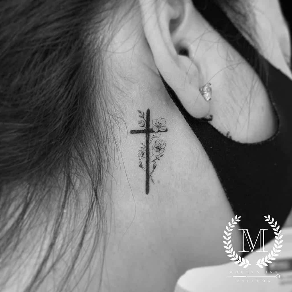 A striking black cross tattoo with elegantly entwined roses graces the area behind the ear