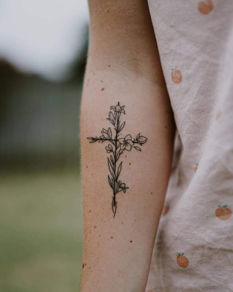 A simple and elegant floral cross tattoo on the forearm, made up of delicate flowers and leaves forming the shape of a cross