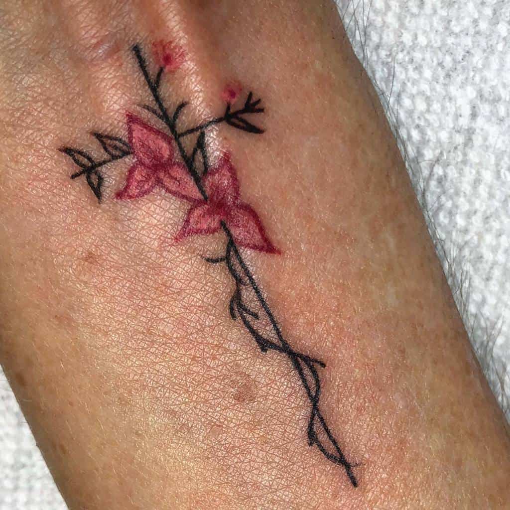 A striking tattoo of a cross adorned with vivid red flowers and dark, intricate leaves