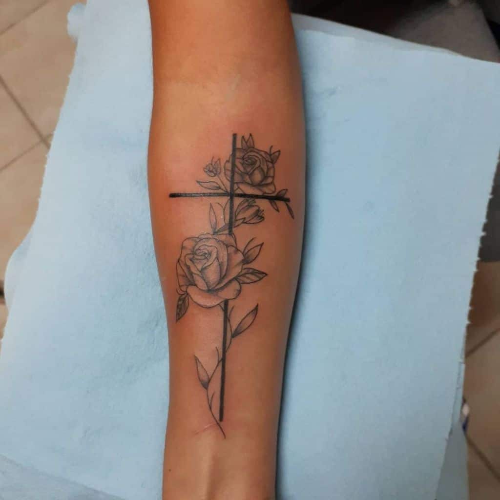 A stunning tattoo of a cross intertwined with vibrant roses graces the forearm