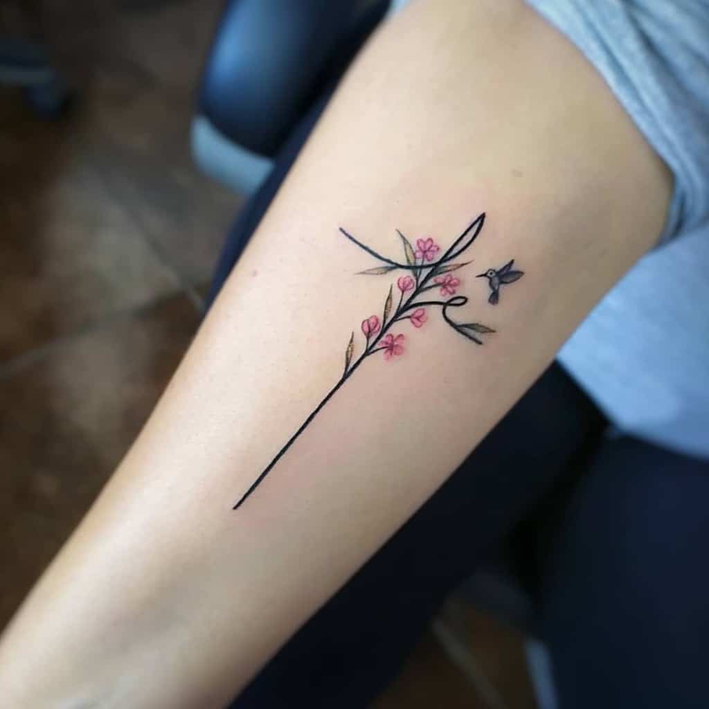 A delicate tattoo featuring a thin branch with pink blossoms and a small hummingbird hovering near, creating a light and graceful design