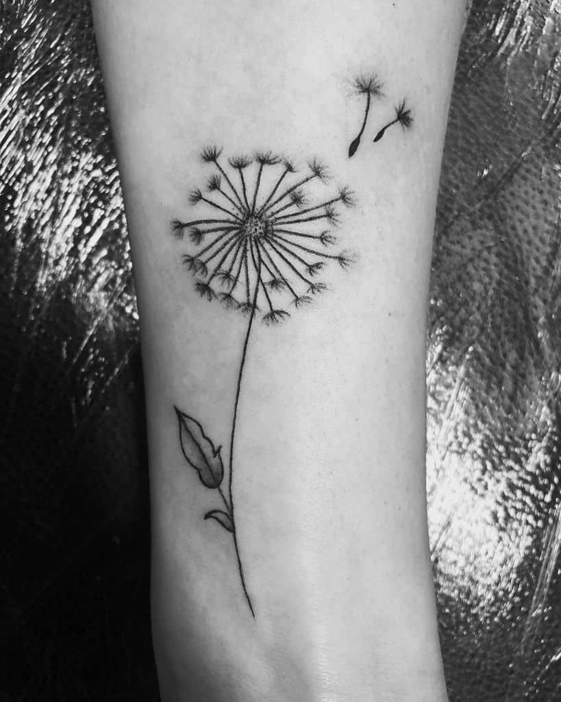 This tattoo depicts a delicate dandelion with seeds drifting away, representing the fleeting nature of time and new beginnings. The fine lines and minimalist design emphasize simplicity and elegance.