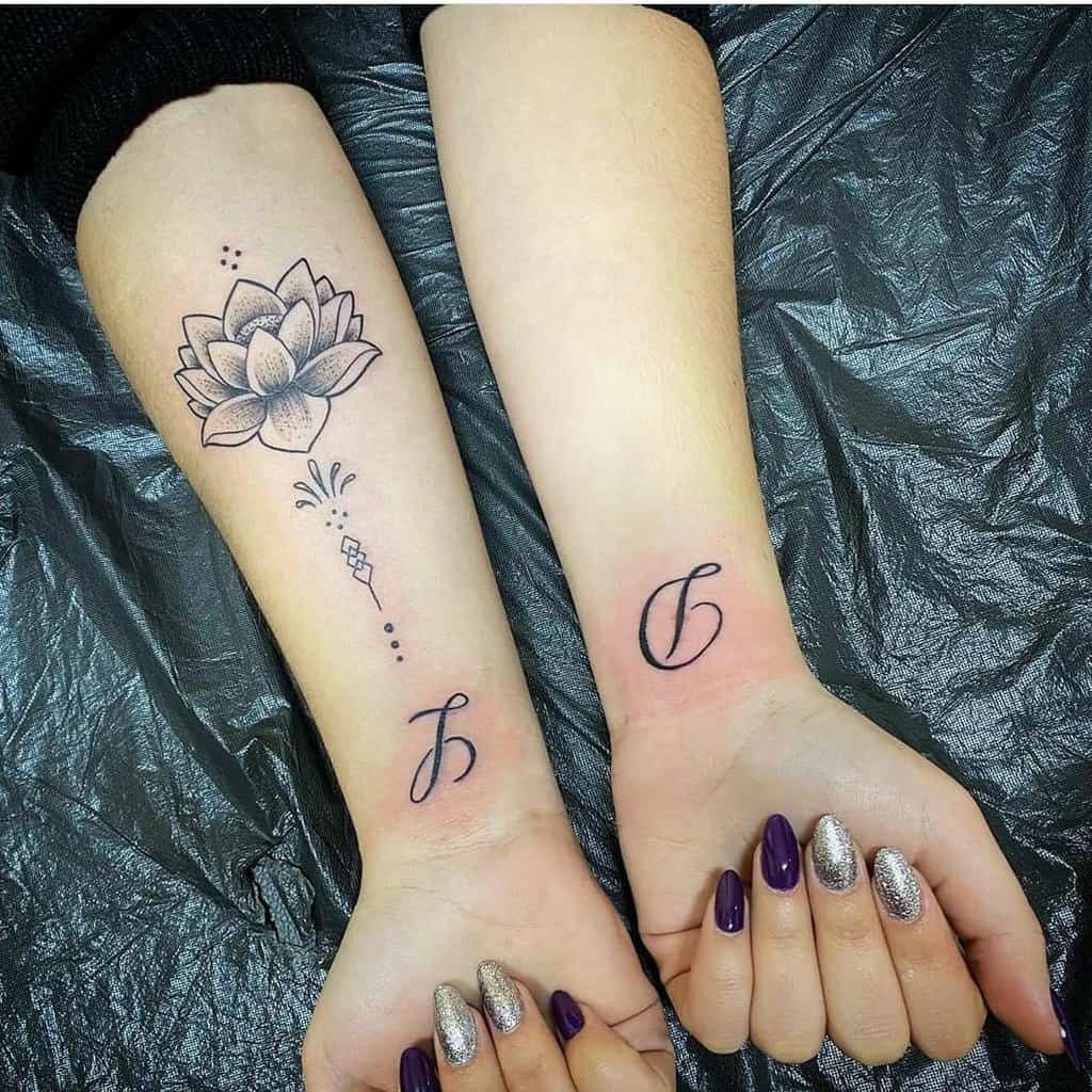 Matching tattoos featuring a lotus flower design on one forearm and elegant initials 'C' and 'J' on the wrists, symbolizing connection