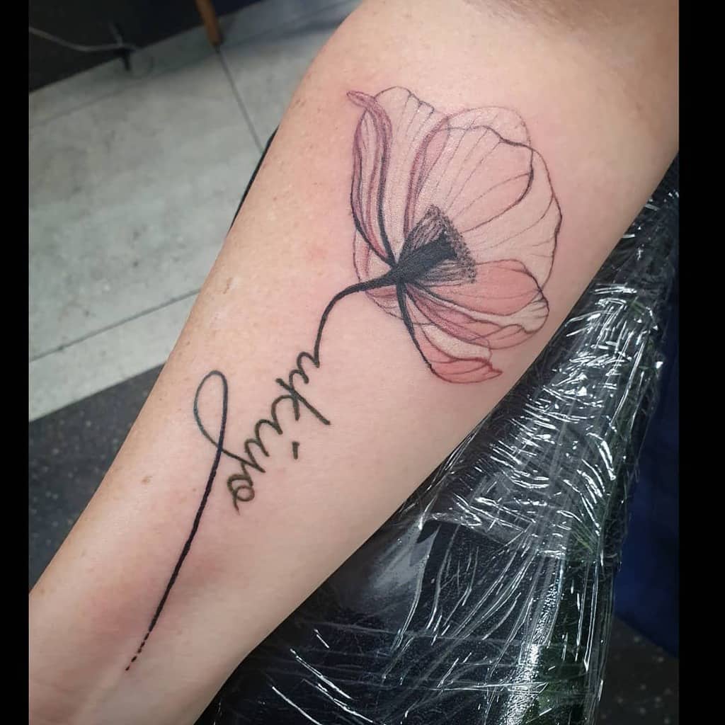 Forearm tattoo of a delicate pink flower with cursive writing as the stem
