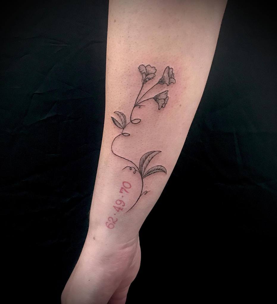 Forearm tattoo of a blooming flower vine with dates in red ink below