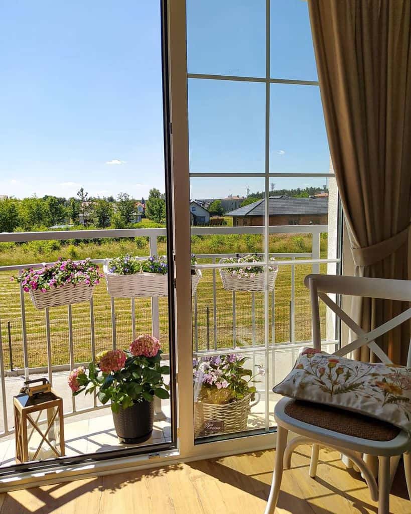 Sunny balcony with potted flowers and hanging baskets, overlooking a green backyard.