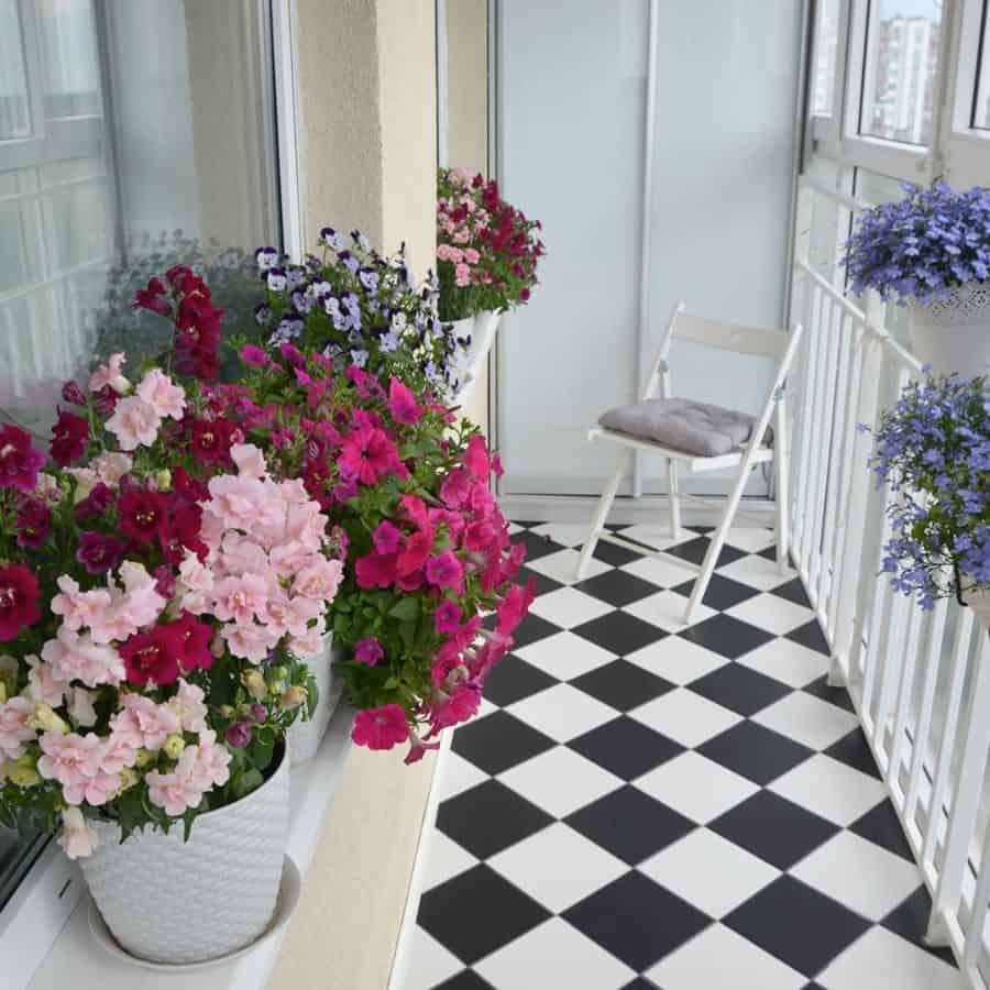 Balcony with vibrant potted flowers and checkered floor, featuring a white folding chair.