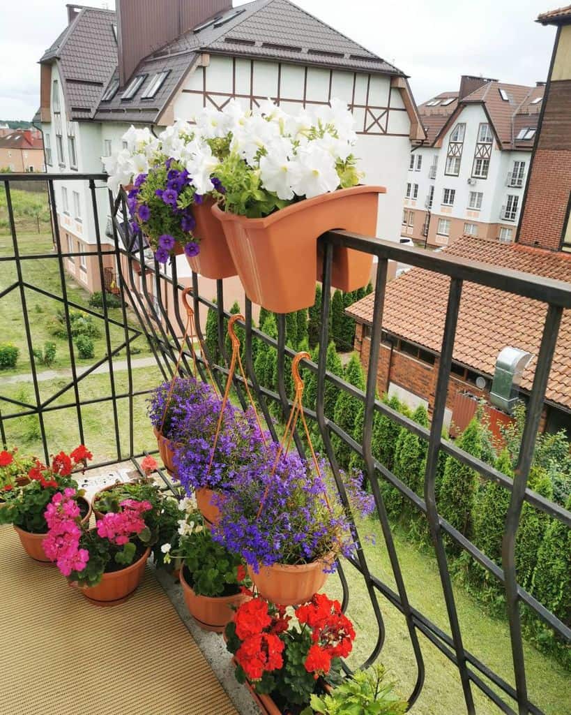 Small balcony with colorful potted flowers and hanging planters, overlooking a green yard.