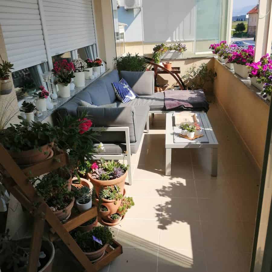 Cozy balcony with grey sectional sofa, potted flowers, and a coffee table decorated with plants.